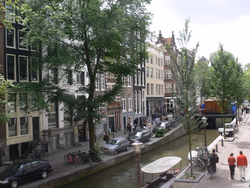 Canal e ruas estreitas do bairro De Wallen em Amsterdã ao entardecer, com fachadas históricas iluminadas e refletidas na água