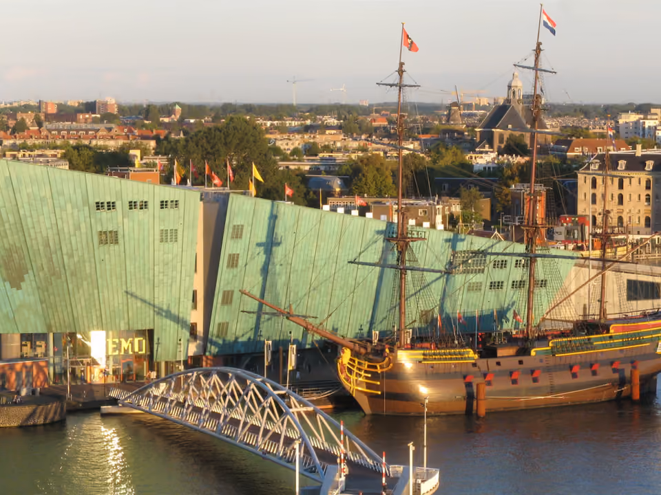 Prédio verde e curvo do NEMO Science Museum em Amsterdã, à beira da água, com o telhado inclinado usado como terraço público