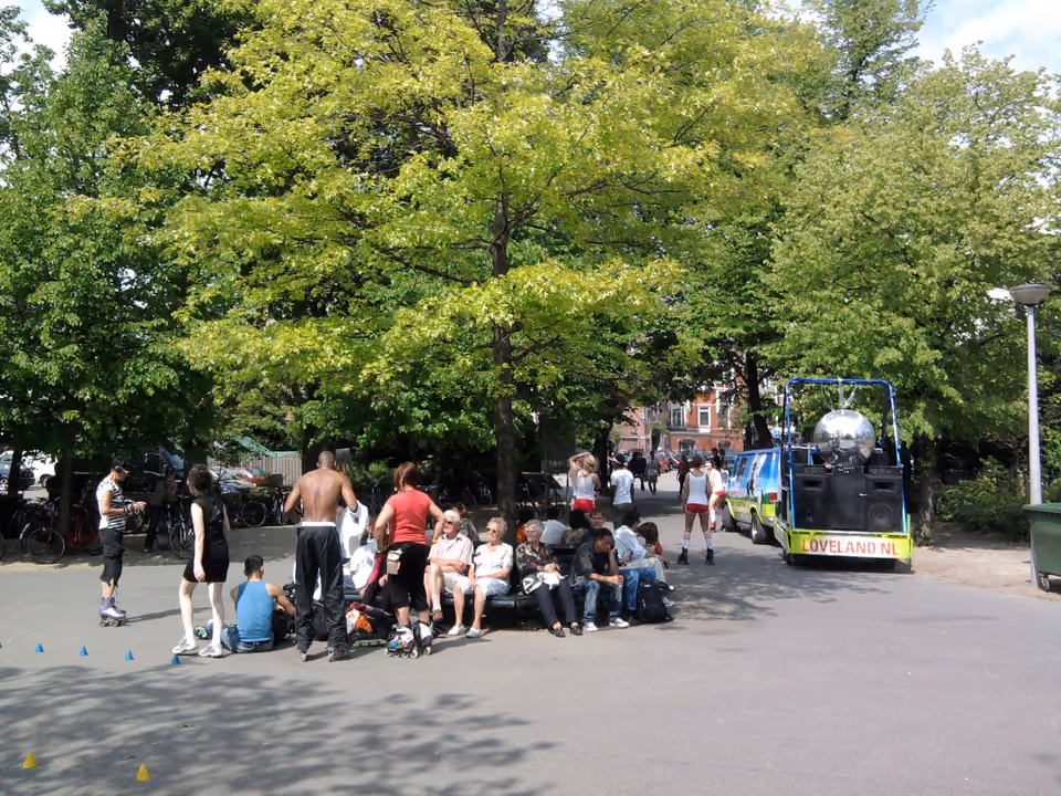 Trilha arborizada dentro do Vondelpark em Amsterdã, com ciclistas e pedestres circulando entre árvores altas e um lago ao fundo