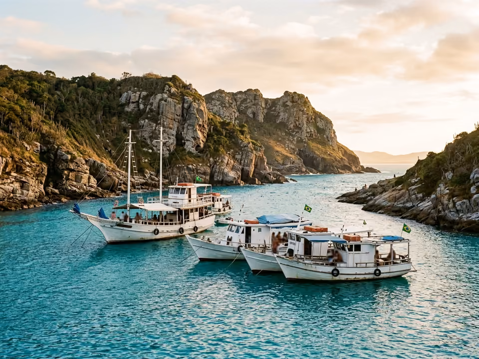 Barcos brancos de passeio ancorados em enseada turquesa cercada de paredões, vistos do mar