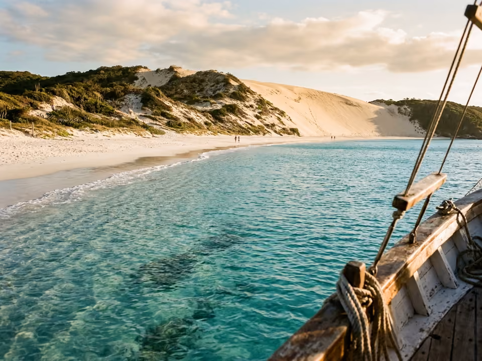 Areia branquíssima da Praia do Farol com duna gigante e água rasa clara, vista de barco ancorado