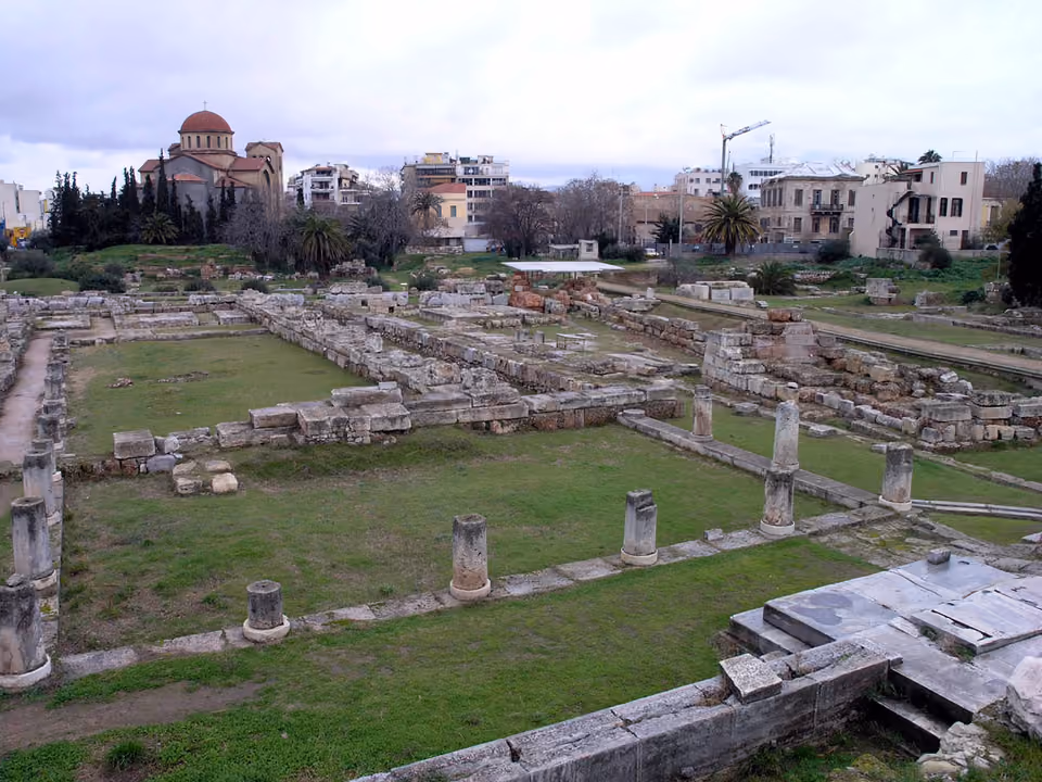 Ruínas e túmulos do antigo cemitério de Kerameikos em Atenas, com vegetação verde ao redor das pedras funerárias