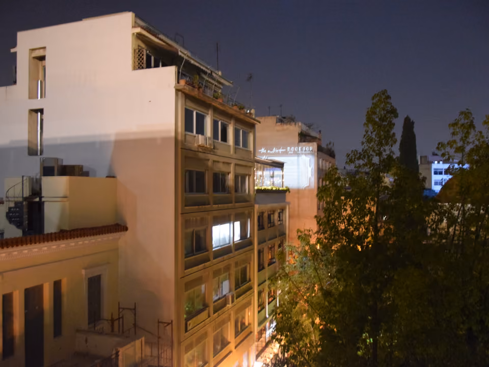 Vista noturna de um bairro boêmio de Atenas, com bar de rooftop iluminado entre os prédios