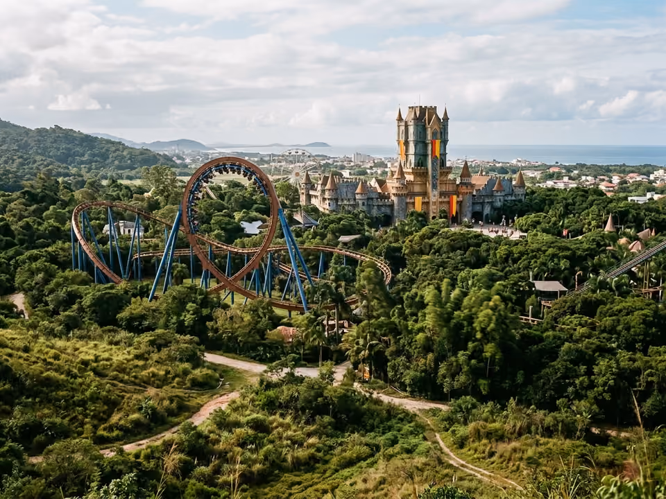 Castelo do parque temático se erguendo acima das árvores com loop de montanha-russa ao lado, em Penha