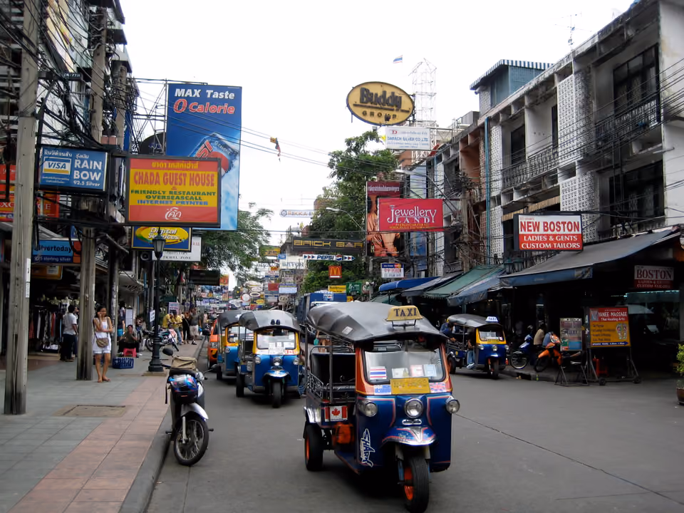 Rua de Khao San, em Bangkok, com tuk-tuks estacionados e letreiro de bar e hospedagem