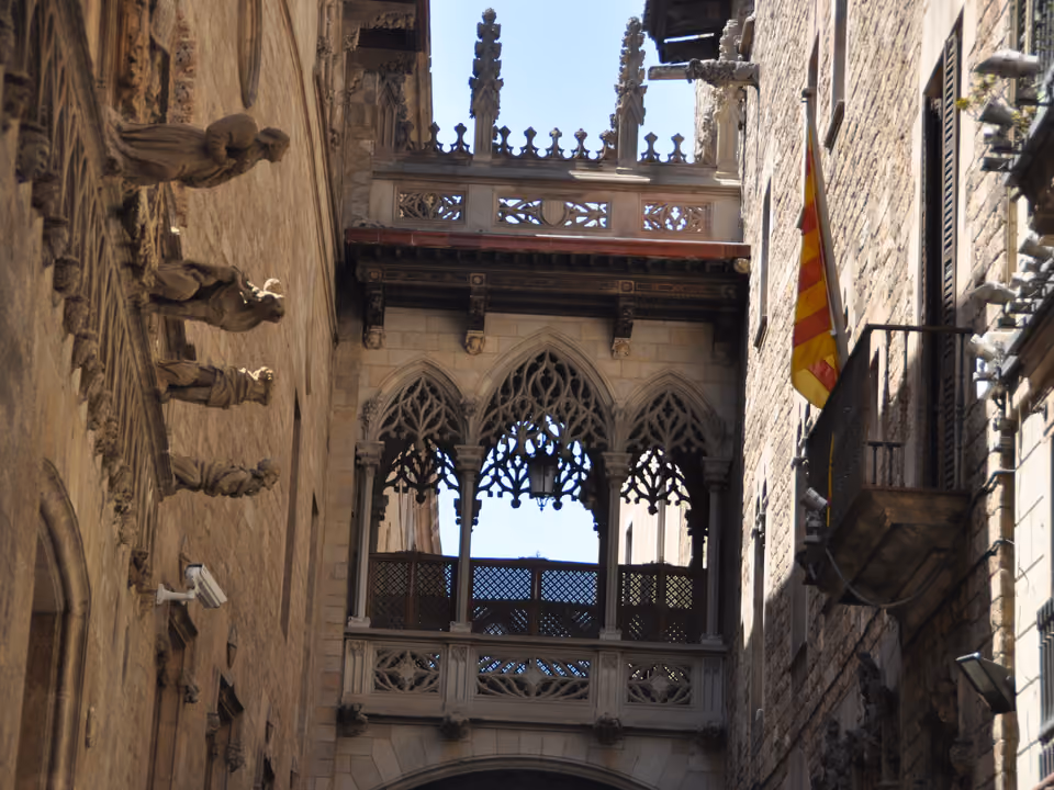 O Pont del Bisbe no Bairro Gótico de Barcelona: o arco de pedra neogótico rendilhado ligando dois prédios sobre a Carrer del Bisbe, com uma bandeira catalã pendurada