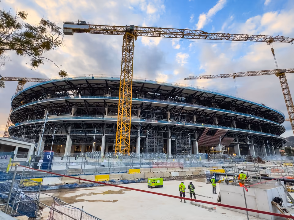 O Spotify Camp Nou em Barcelona em obras, em dezembro de 2025, com a arquibancada superior aberta, guindastes ao redor e operários de colete no canteiro em primeiro plano