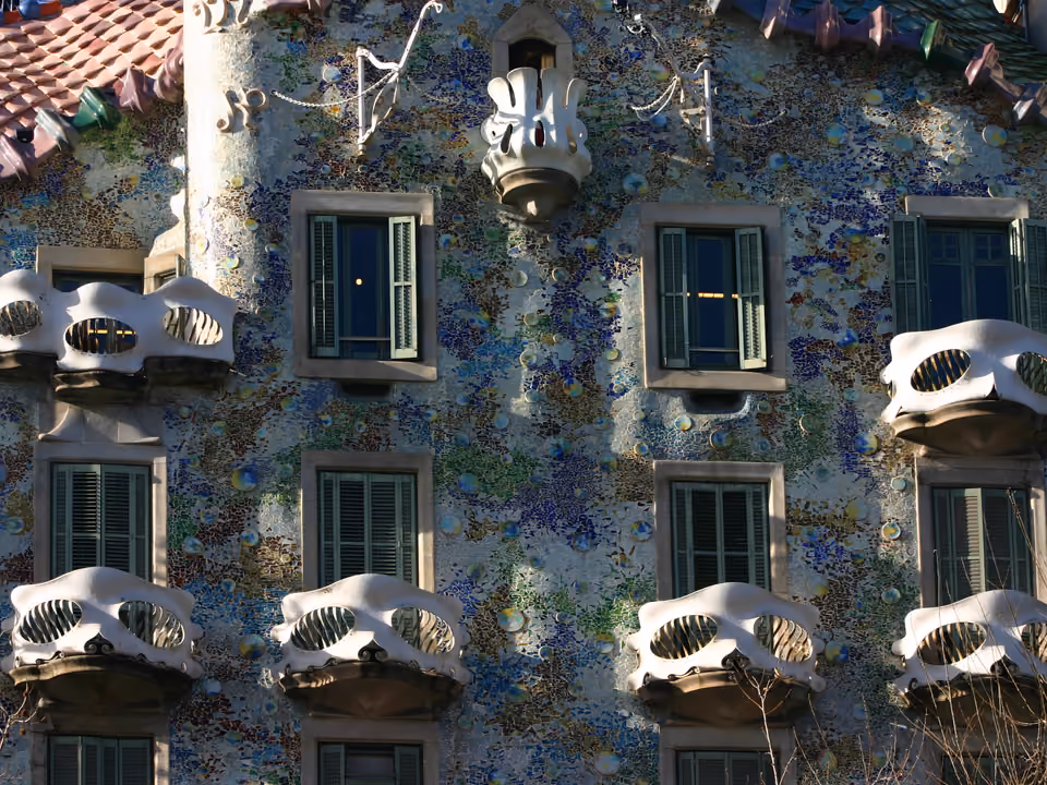 Detalhe da fachada da Casa Batlló em Barcelona: as varandas em forma de máscara de ferro, o mosaico ondulado em tons de azul, verde e ouro e o começo do telhado escamado no alto