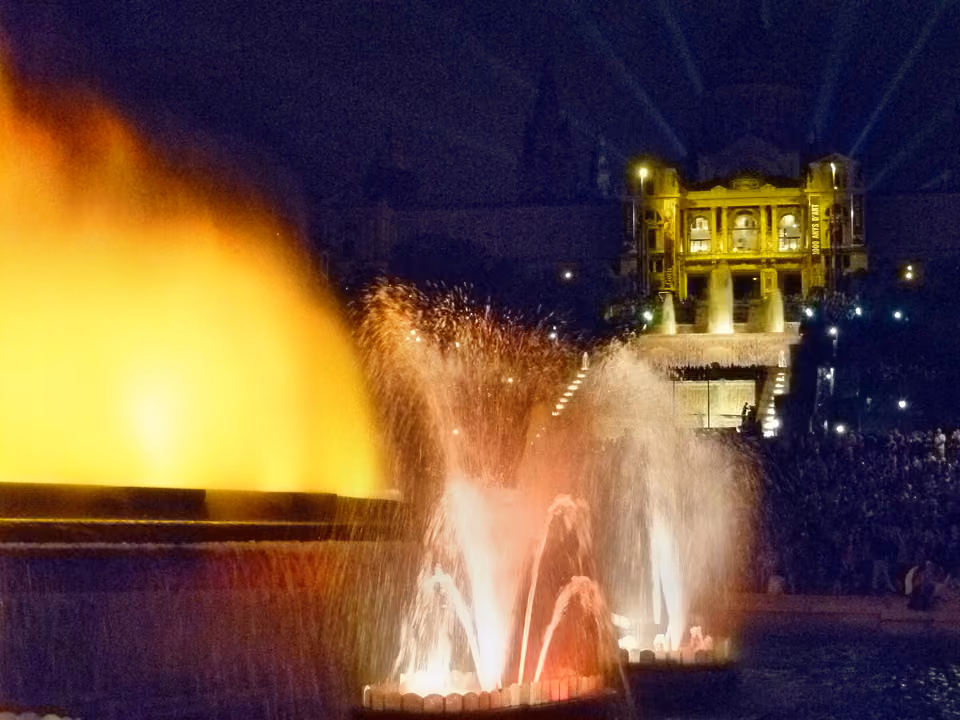 Fonte Mágica de Montjuïc em Barcelona durante o espetáculo noturno, com jatos d'água iluminados de laranja e o Palácio Nacional dourado ao fundo