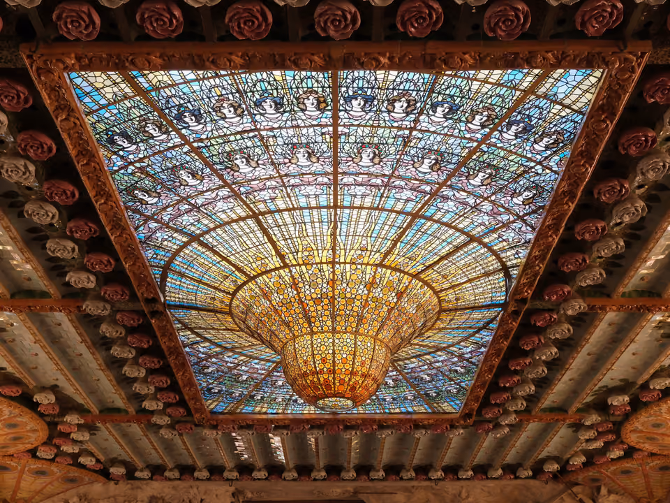 Interior do Palau de la Música Catalana em Barcelona, com a claraboia invertida de vitral colorido em forma de sino dourado no teto da sala de concertos, cercada de rosas de cerâmica