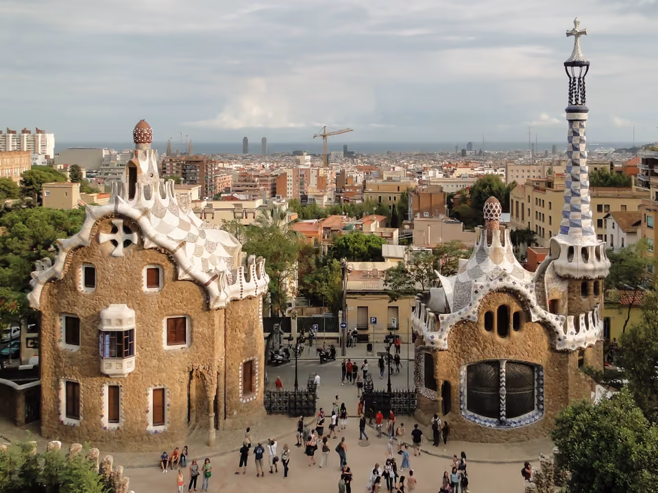 As duas casas-guarda de conto de fadas na entrada do Park Güell em Barcelona, com telhados de mosaico (trencadís) e a torre da cruz, e a cidade até o mar ao fundo