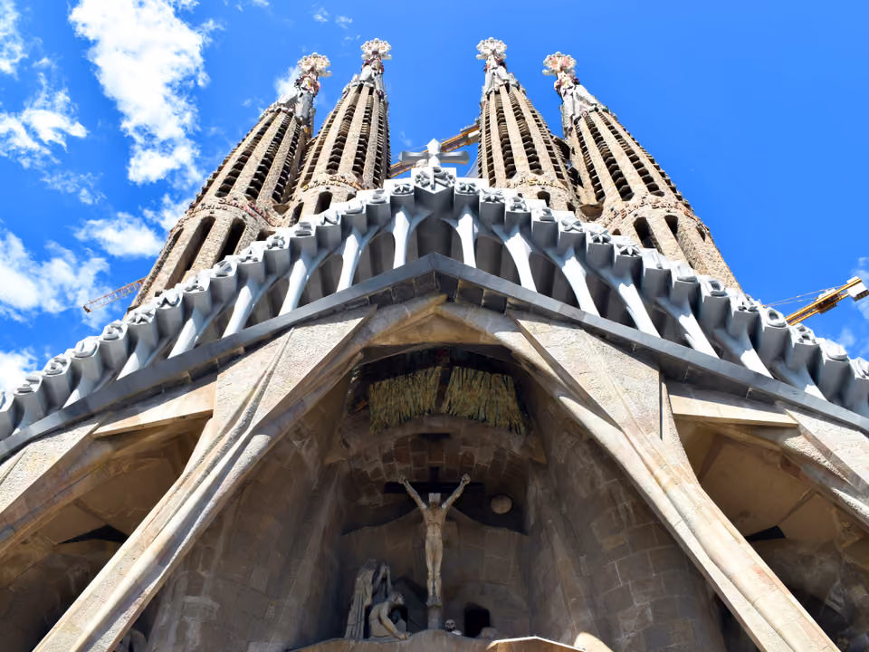Fachada da Paixão da Sagrada Família em Barcelona vista de baixo, com as esculturas angulares de Subirachs, o pórtico inclinado sobre colunas e as quatro torres pontudas