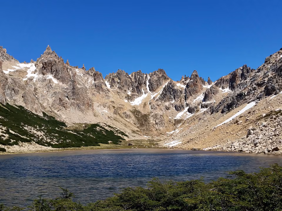 Maciço do Cerro Catedral em Bariloche, picos rochosos com manchas de neve acima da linha de floresta, e um lago na base