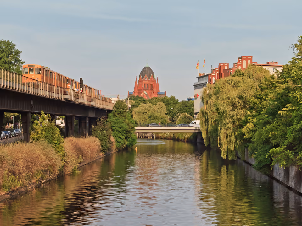 Canal Landwehrkanal no bairro Kreuzberg em Berlim, com um trem de metrô elevado e a torre da igreja ao fundo