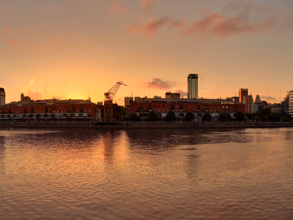 Diques de Puerto Madero ao entardecer, armazéns de tijolo restaurados, guindaste histórico e prédios de vidro ao fundo