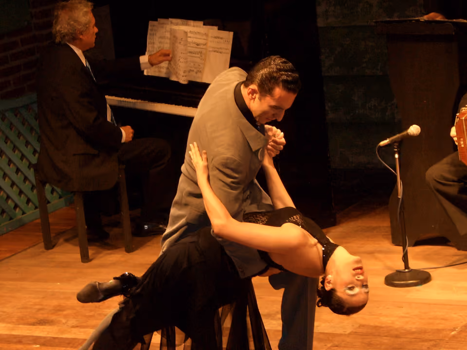 Casal dançando tango no palco de uma casa de espetáculo em Buenos Aires, com pianista e bandoneonista ao fundo