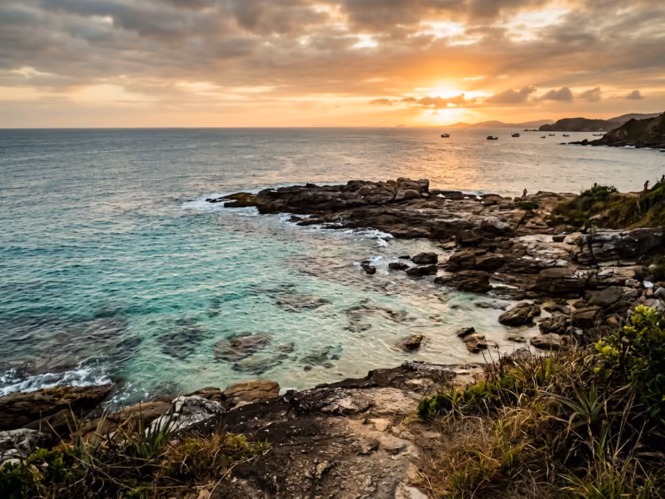 Ponta rochosa baixa do Pai Vitório com água rasa transparente e mar aberto ao pôr do sol