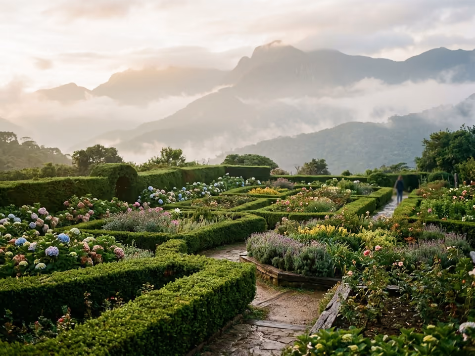 Jardins desenhados do Amantikir com cercas-vivas esculpidas, canteiros floridos e montanhas na névoa