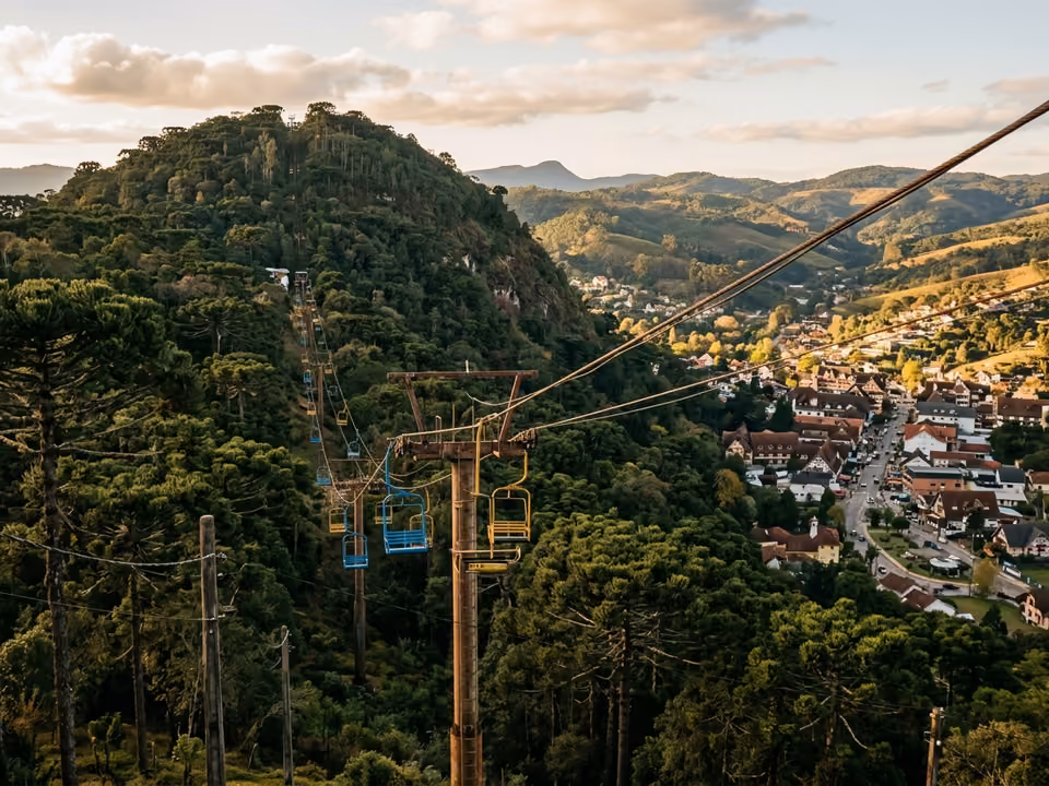 Cadeirinhas do teleférico subindo o Morro do Elefante sobre a mata, com a cidade no vale