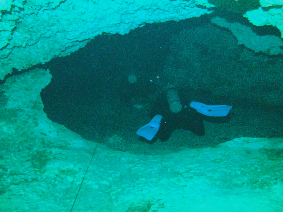Interior do sistema de cavernas do Cenote Dos Ojos, com água azul translúcida e formações de estalactites visíveis por cima e por baixo da superfície