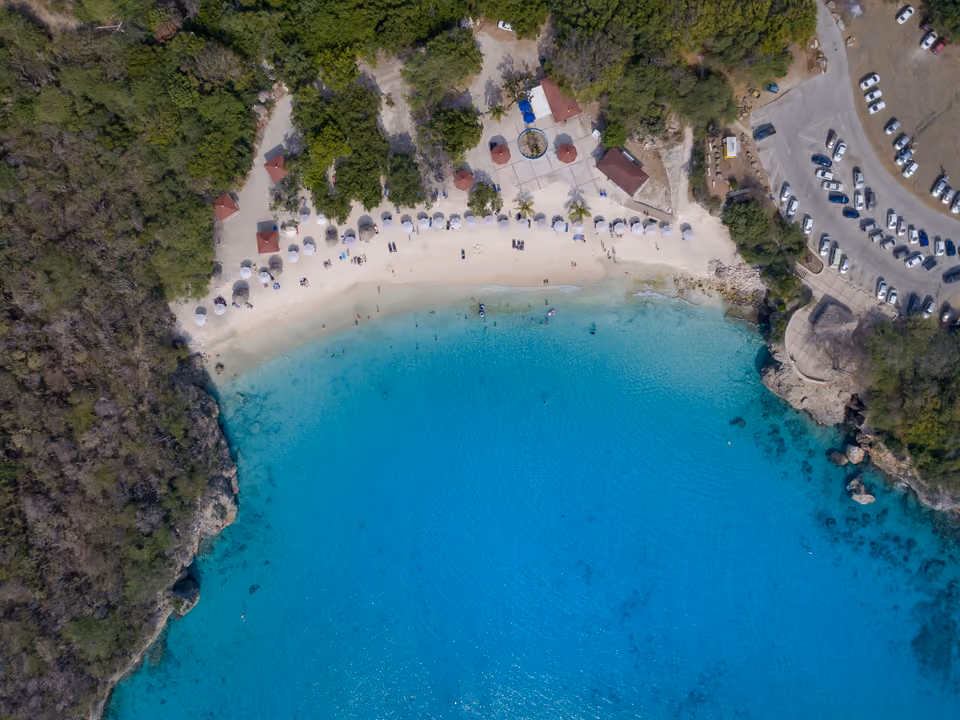 Vista aérea da enseada de Playa Kenepa Grandi, com água turquesa, areia clara e estacionamento