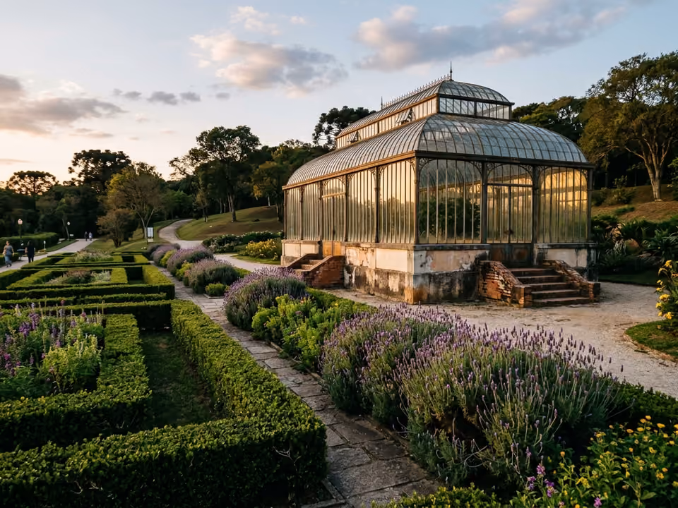 Estufa de vidro do Jardim Botânico de Curitiba vista em ângulo lateral, entre canteiros de lavanda e cercas-vivas