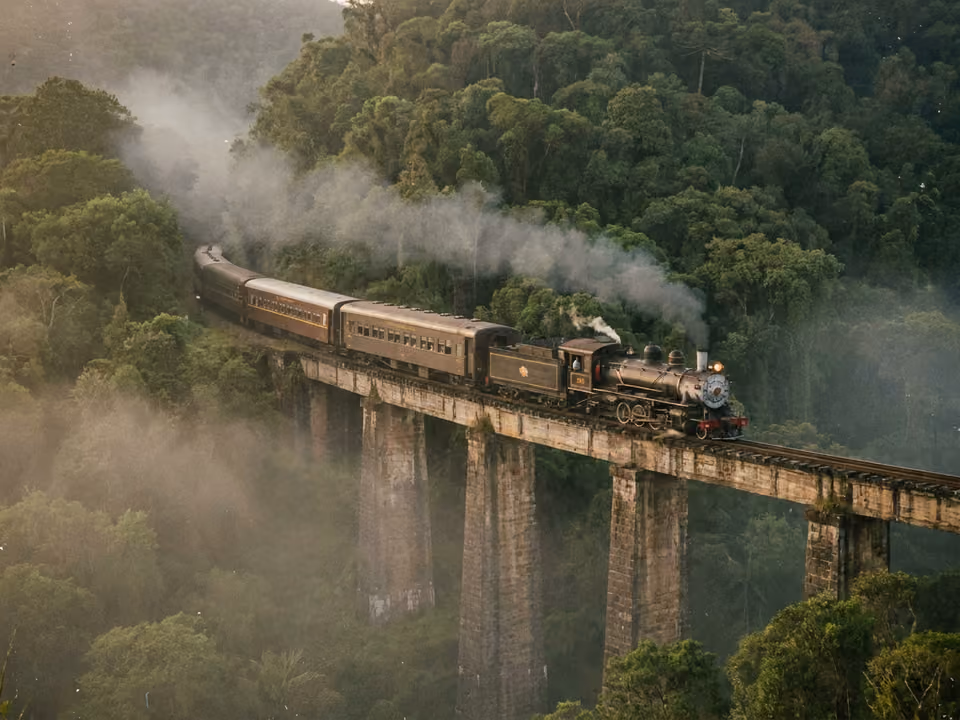 Trem turístico cruzando viaduto de pedra na Serra do Mar, entre mata atlântica e névoa