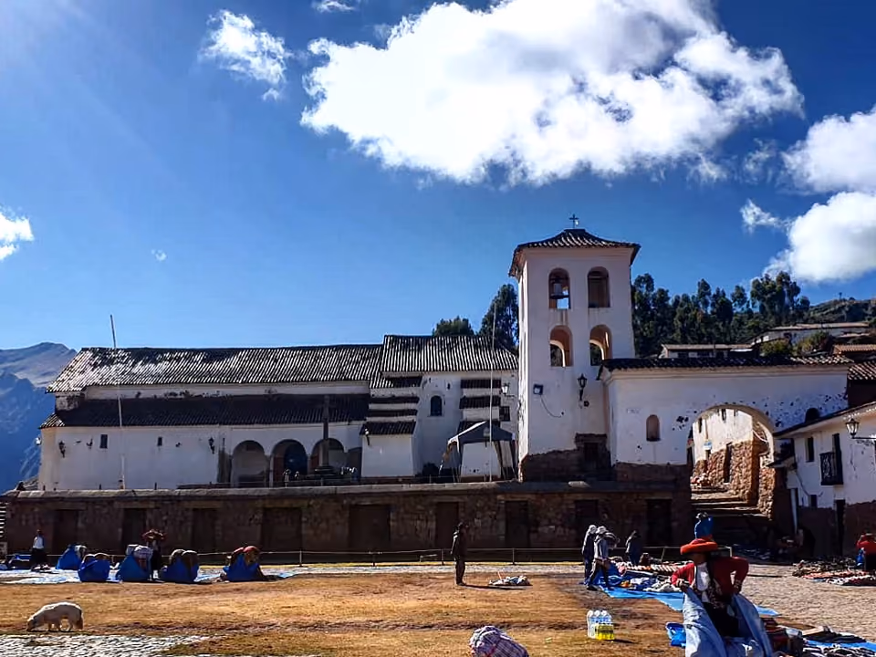 Igreja colonial de Chinchero com torre sineira, construída sobre fundações de pedra inca, com barracas de tecelagem na praça em frente