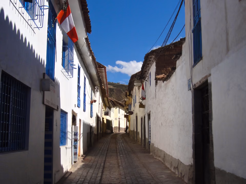 Ladeira estreita de pedra no bairro de San Blas, em Cusco, com casario colonial branco e telhados de telha