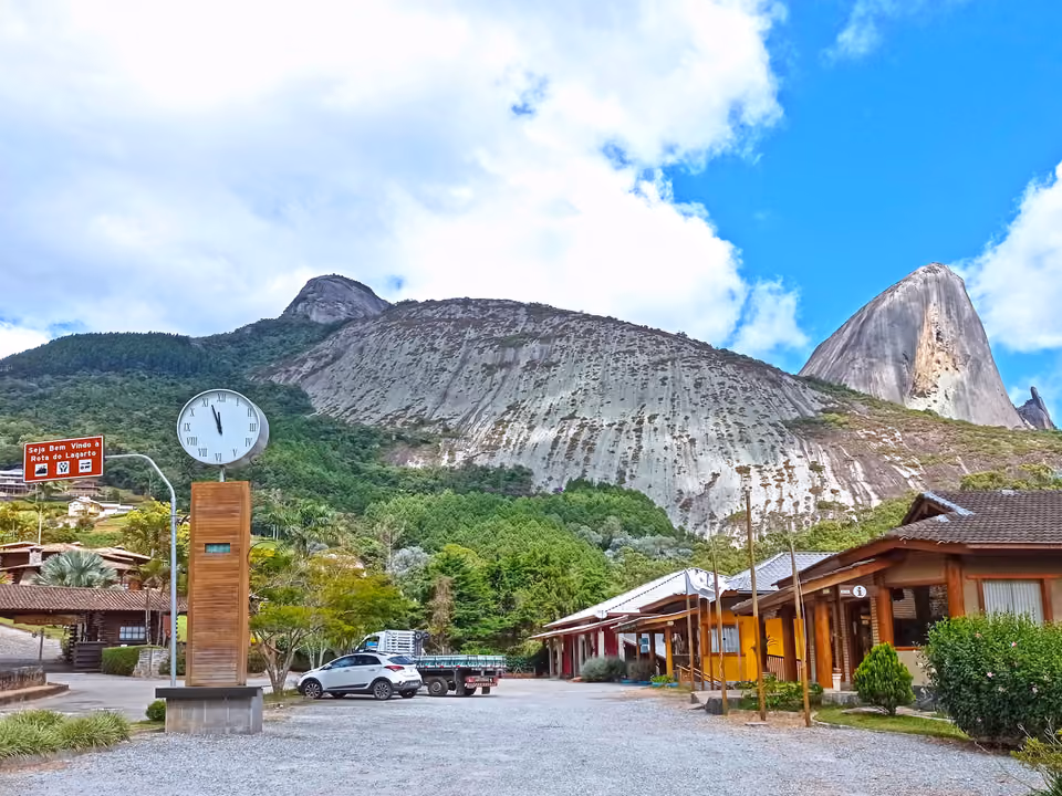 Entrada da Rota do Lagarto, com relógio, comércio local e a Pedra Azul ao fundo