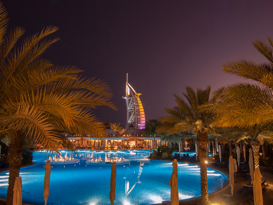 Burj Al Arab iluminado à noite, visto de uma piscina cercada por coqueiros