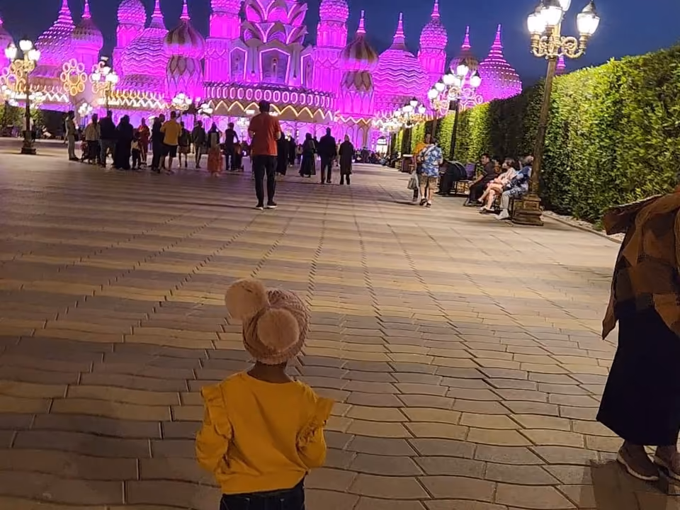 Pavilhão iluminado em tons de rosa e roxo no Global Village, em Dubai, com visitantes caminhando à noite