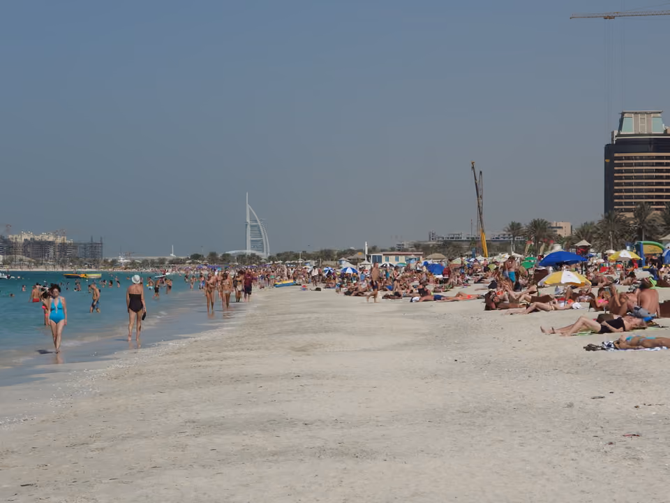 Praia de Jumeirah (JBR) com banhistas na areia e o Burj Al Arab visível ao longe