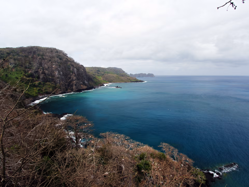 Baía dos Golfinhos em Fernando de Noronha vista do alto, a enseada fechada de água azul-escura entre paredões cobertos de mata