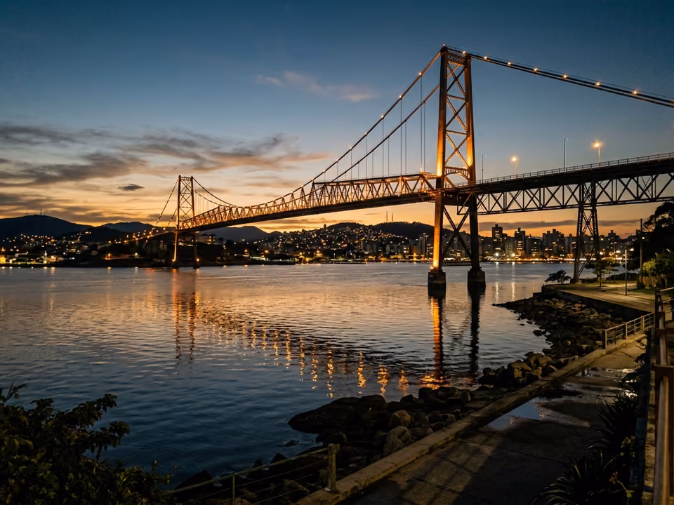 Ponte Hercílio Luz iluminada ao anoitecer, com a estrutura de aço refletida na baía calma