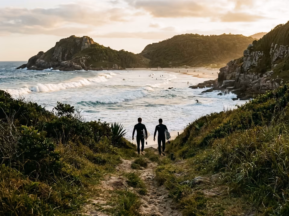Descida de capim para a Praia Mole com silhuetas de surfistas e ondas fortes entre costões