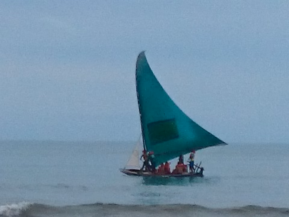Jangada com vela verde navegando no mar de Canoa Quebrada, no Ceará, com passageiros a bordo