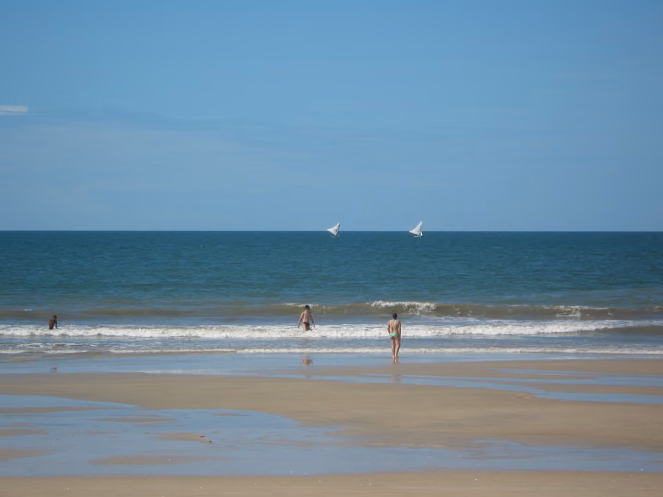 Praia das Fontes, no Ceará, com banhistas no mar aberto e jangadas ao longe no horizonte
