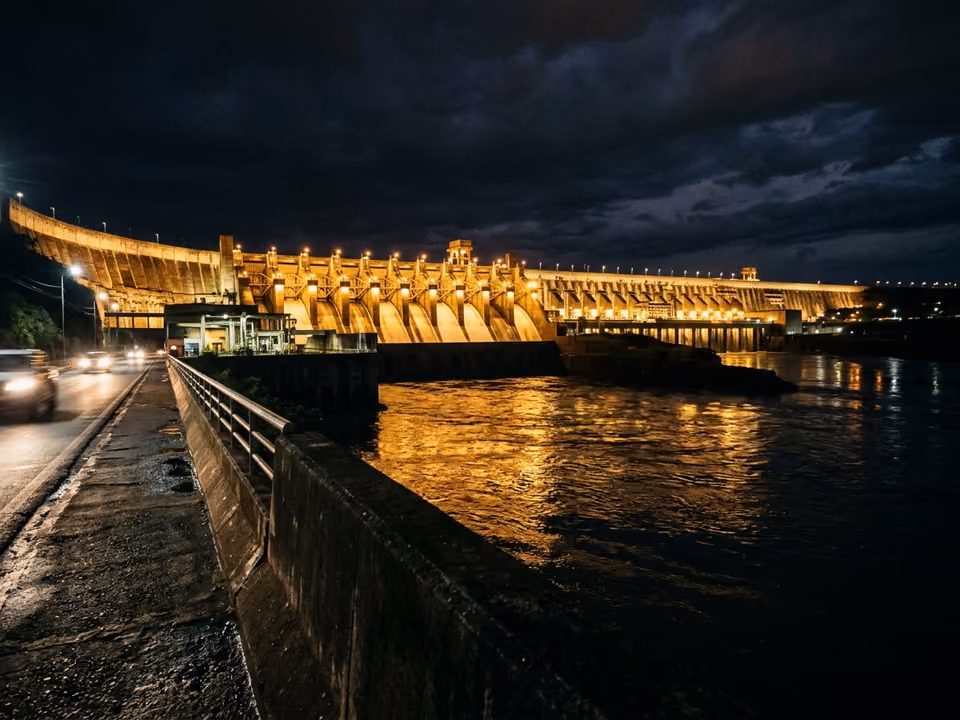 Barragem de Itaipu iluminada à noite com luzes douradas refletidas no rio Paraná