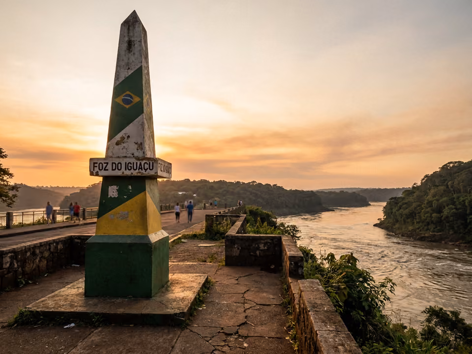 Obelisco verde e amarelo do Marco das Três Fronteiras ao pôr do sol, com o encontro dos rios ao lado
