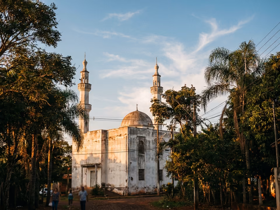 Mesquita branca de dois minaretes e cúpula emoldurada por árvores tropicais