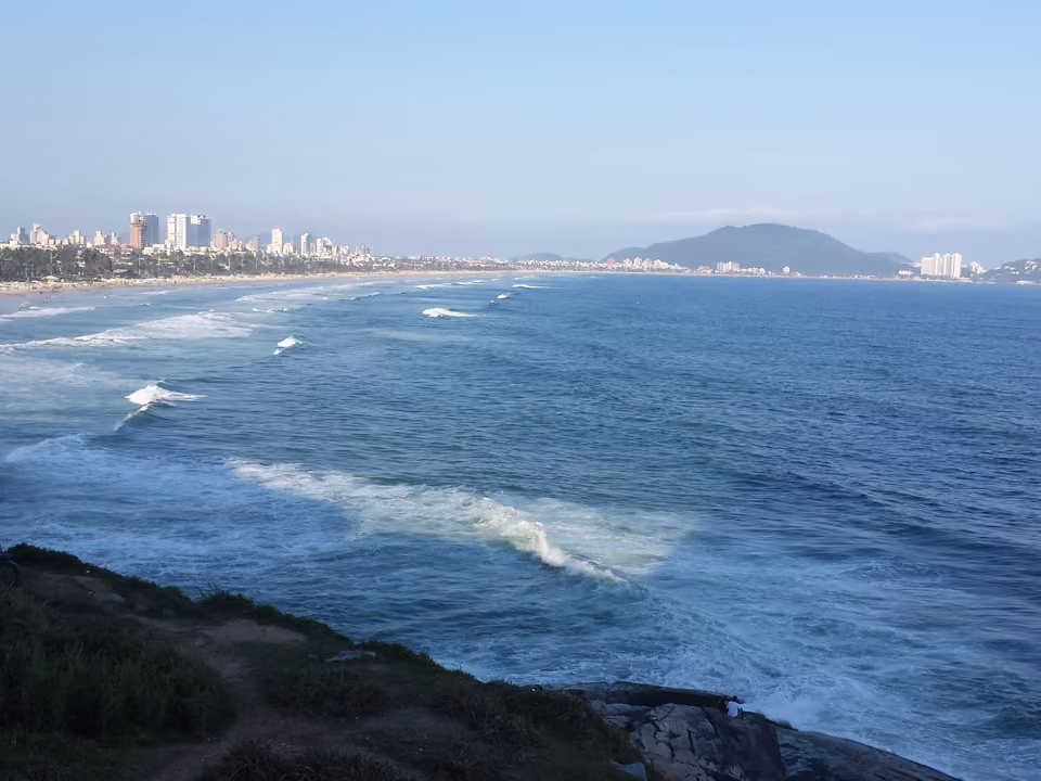 Vista da Praia da Enseada com ondas e skyline de Guarujá ao fundo