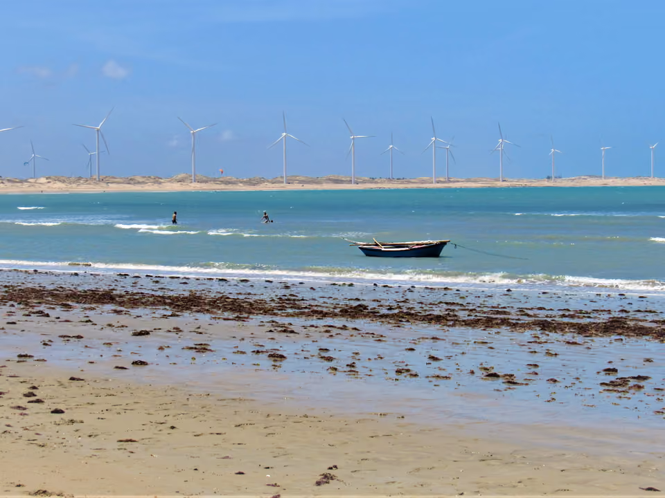Barco de pescador na praia, com dunas e turbina eólica ao fundo, litoral de Amontada, Ceará