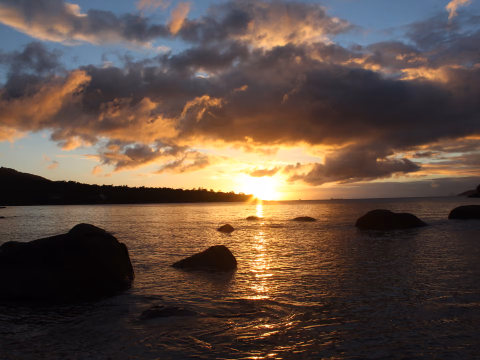 Praia do Julião em Ilhabela, ao pôr do sol, com águas calmas e mata atlântica ao redor