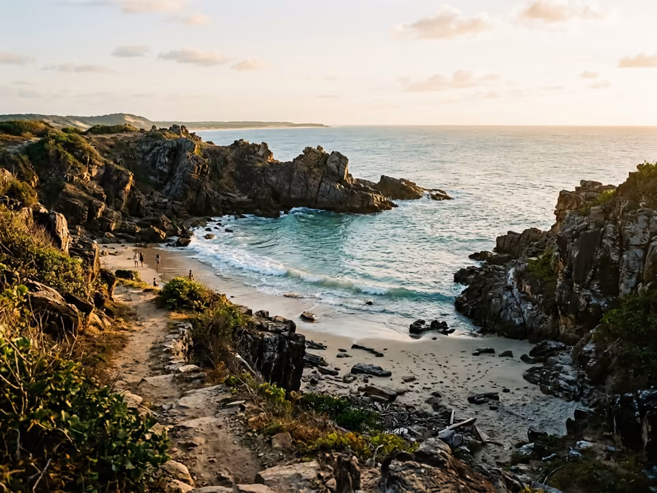 Enseada da Praia da Malhada vista da trilha, com formações rochosas escuras e mar claro
