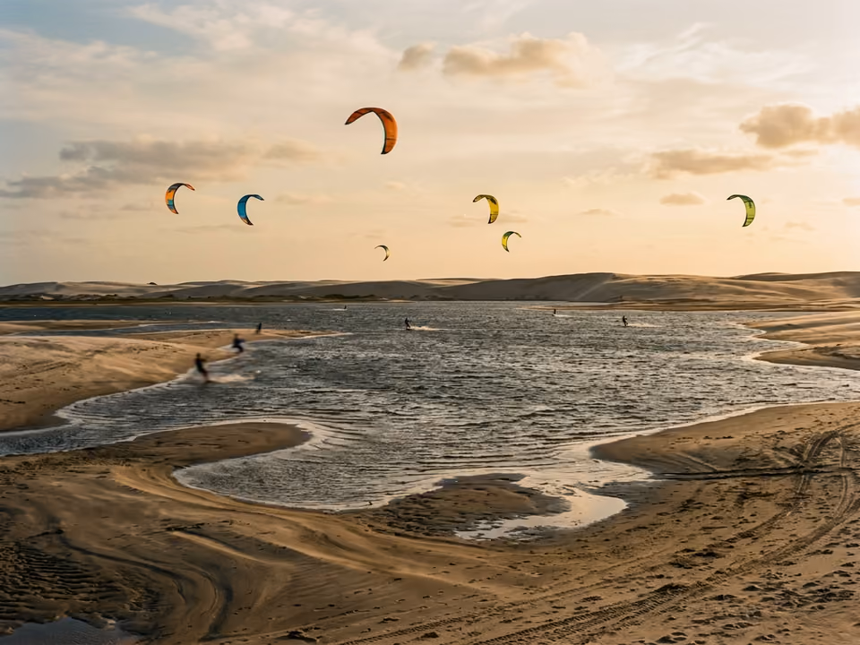 Kites coloridos sobre a água plana e os bancos de areia varridos pelo vento perto de Atins