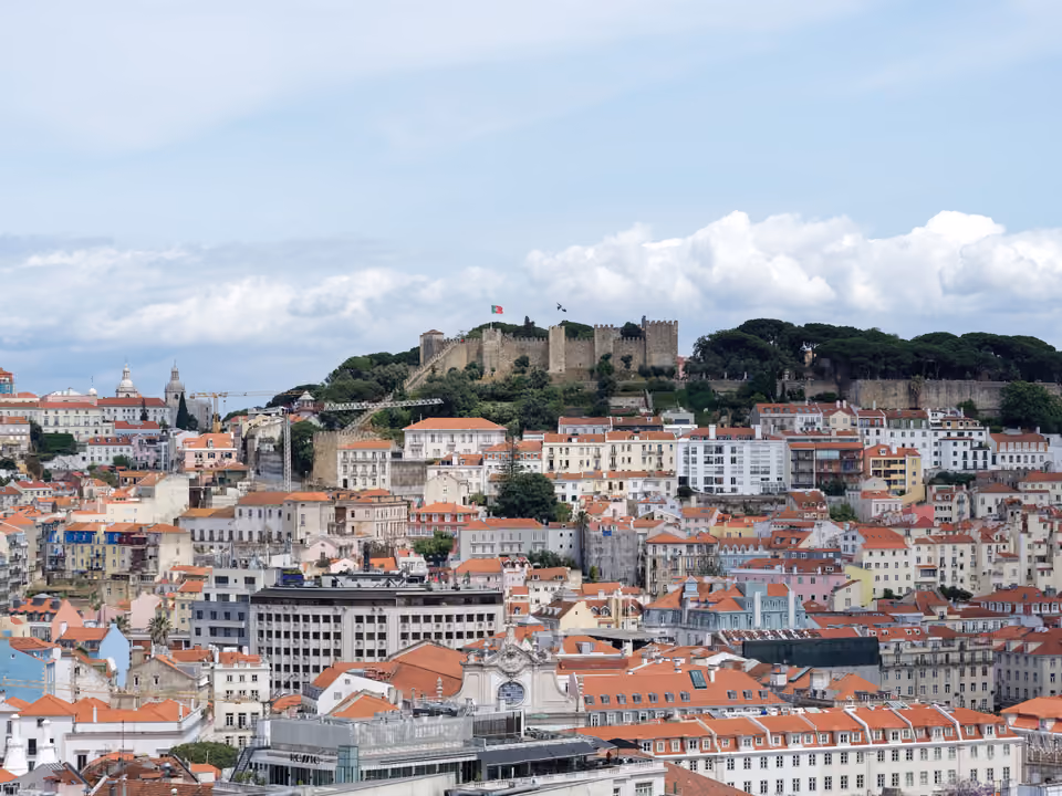Castelo de São Jorge no alto da sua colina sobre o mar de telhados de Lisboa, muralhas ameadas e a bandeira de Portugal hasteada