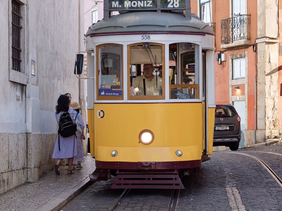 O elétrico 28, bonde amarelo de Lisboa (destino M. Moniz), descendo uma rua estreita de paralelepípedo entre prédios em tons pastel