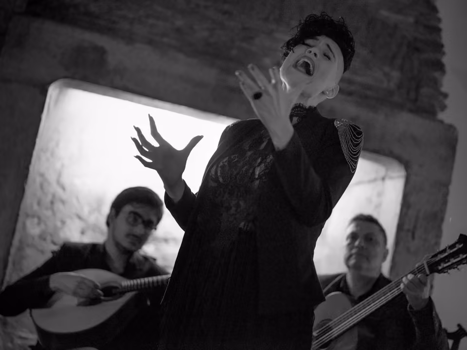 Fadista cantando de olhos fechados numa casa de fado de Lisboa, sob luz baixa, entre a guitarra portuguesa e a viola