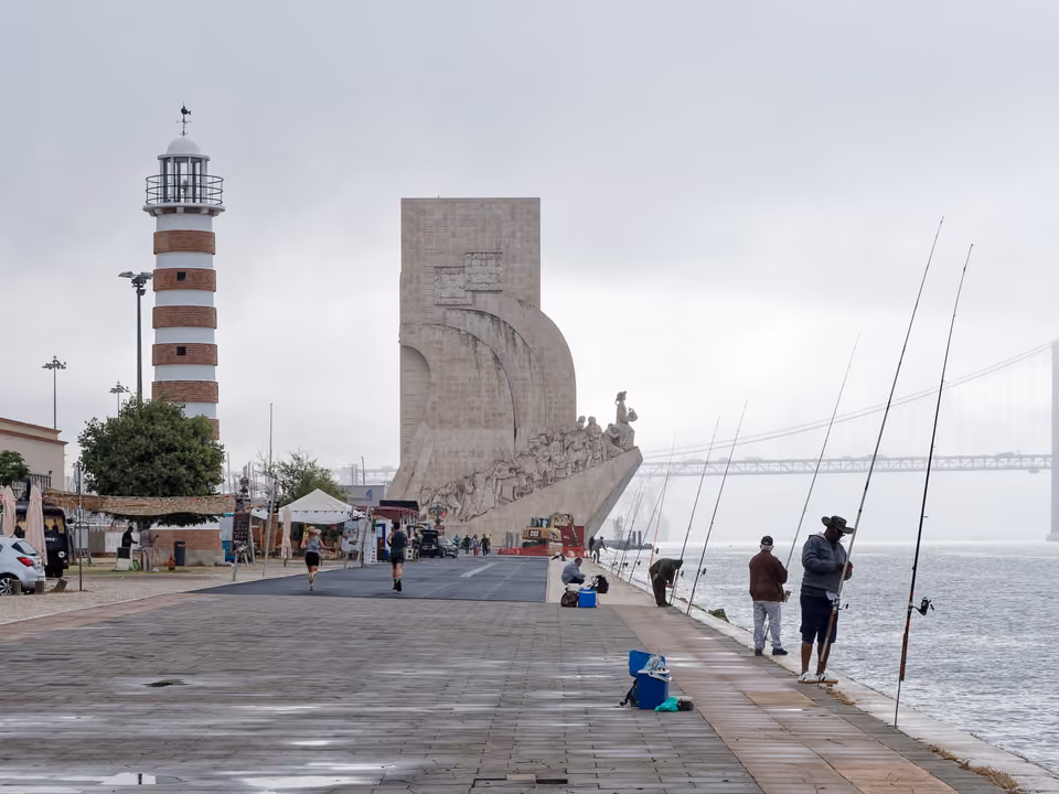 Padrão dos Descobrimentos em Lisboa, monumento de pedra em forma de proa de caravela à beira do Tejo, com o Farol de Belém à esquerda e a ponte 25 de Abril ao fundo